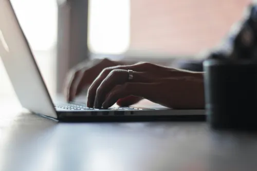 Person typing on their laptop with a silver ring on their left wedding ring finger.