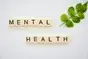 Mental Health spelled out in Scrabble tiles with a piece of greenery next to it.